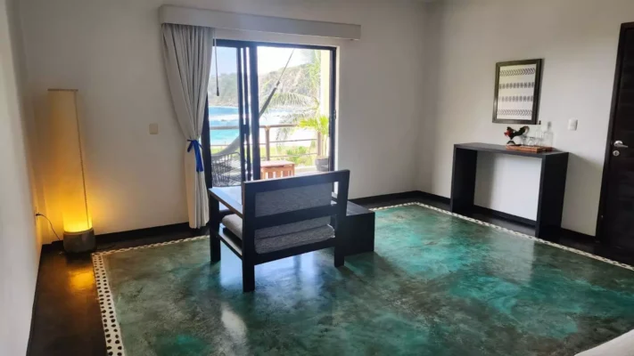 Photo of a room in Hotel Manta Raya with a chair, a table, and a sliding glass door leading out to a balcony that overlooks Playa Salchi, Oaxaca